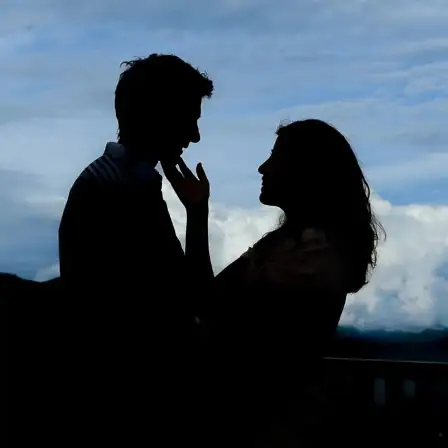 Silhouette of a romantic couple standing close and touching foreheads against a cloudy sky background in Ticino, Switzerland.